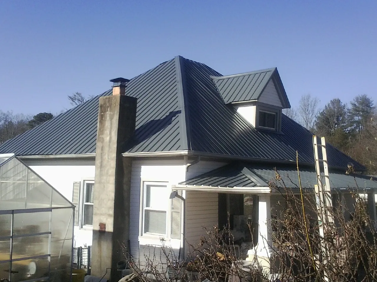 Dark blue standing seam metal roof on a white farmhouse with dormer — Slate & Tile Roof Repair by Roofing Brothers in State Farm