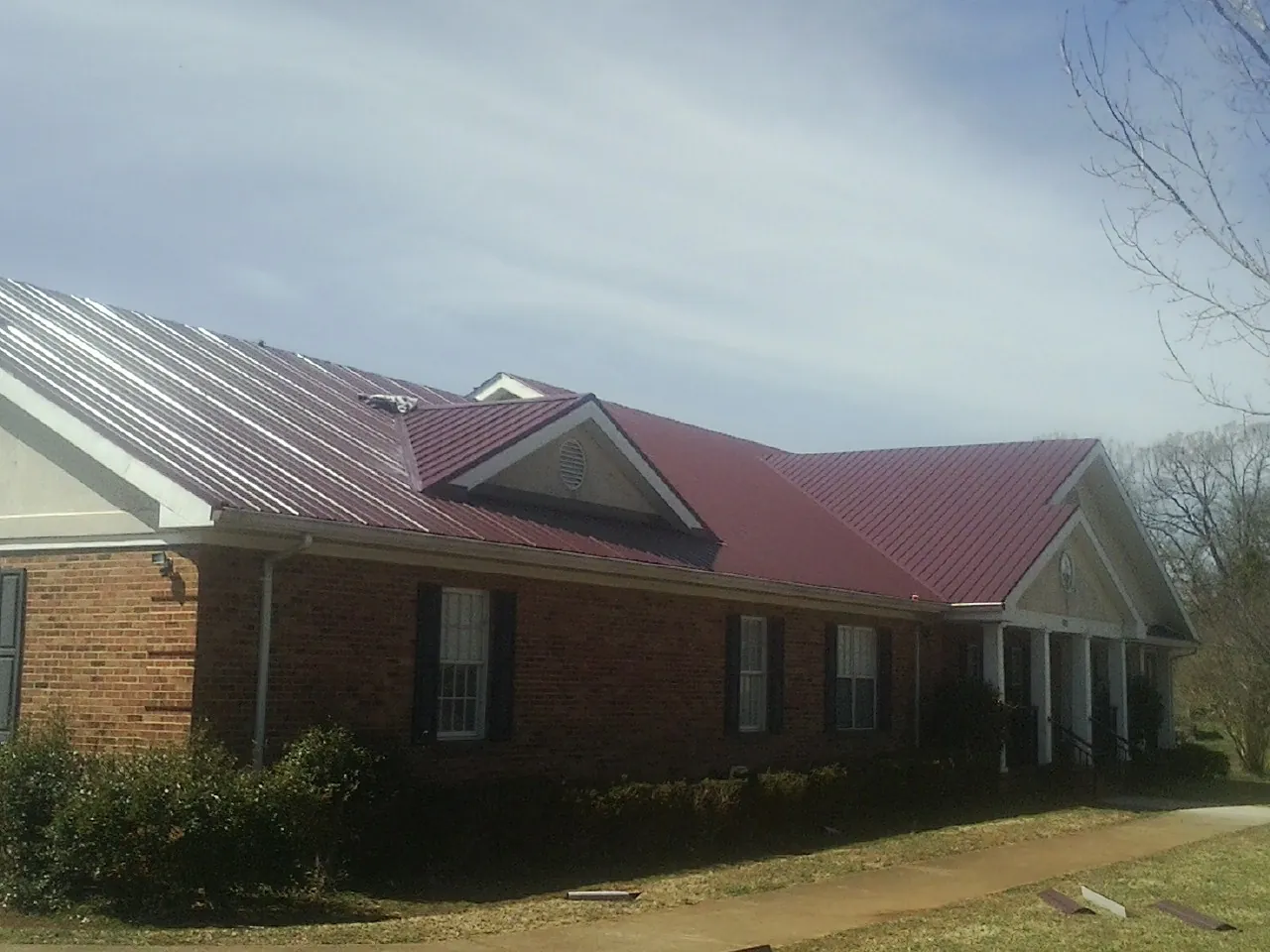 Red metal roof with gabled entries on a long brick building, from a Hail Damage Roof Repair job in State Farm