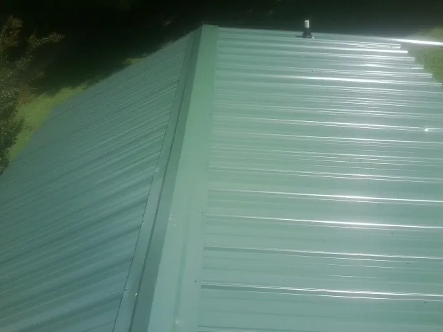 New green metal panels meeting at the ridge of a roof — Flat Roof Repair work by our crew in State Farm