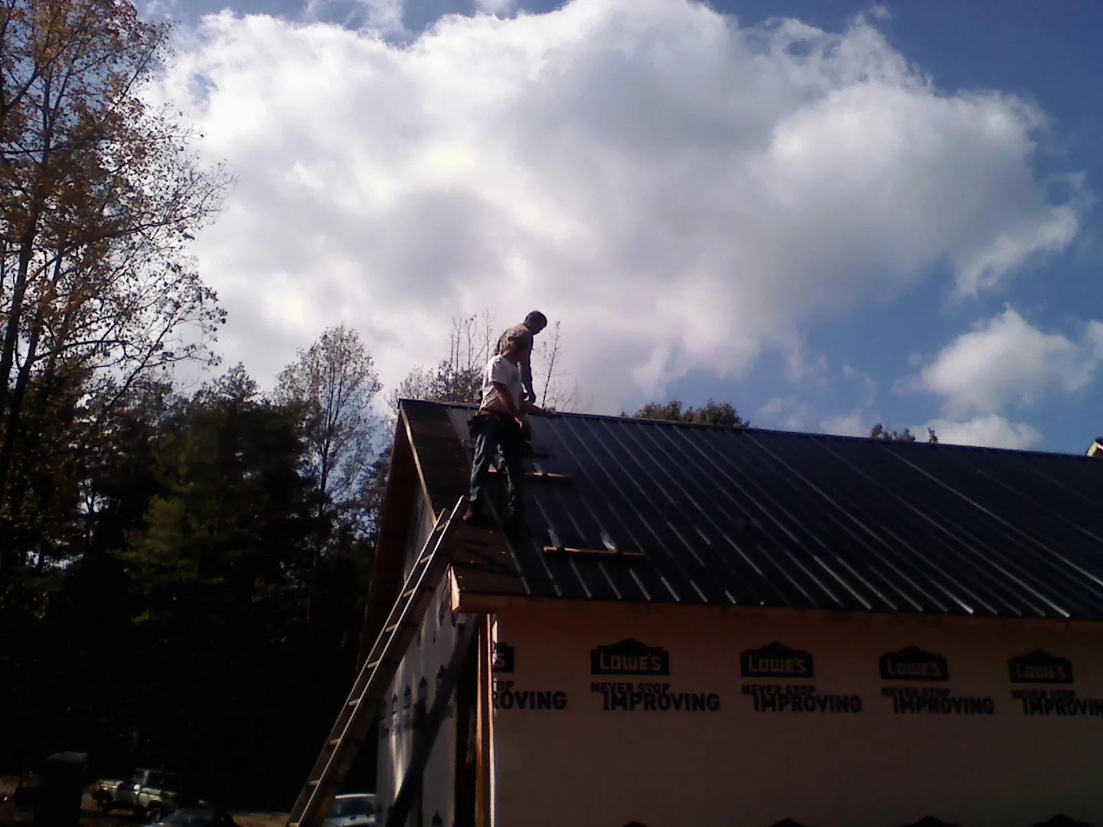 Roofer fastening dark metal panels high against a cloudy sky, from a Roof Inspection job in State Farm