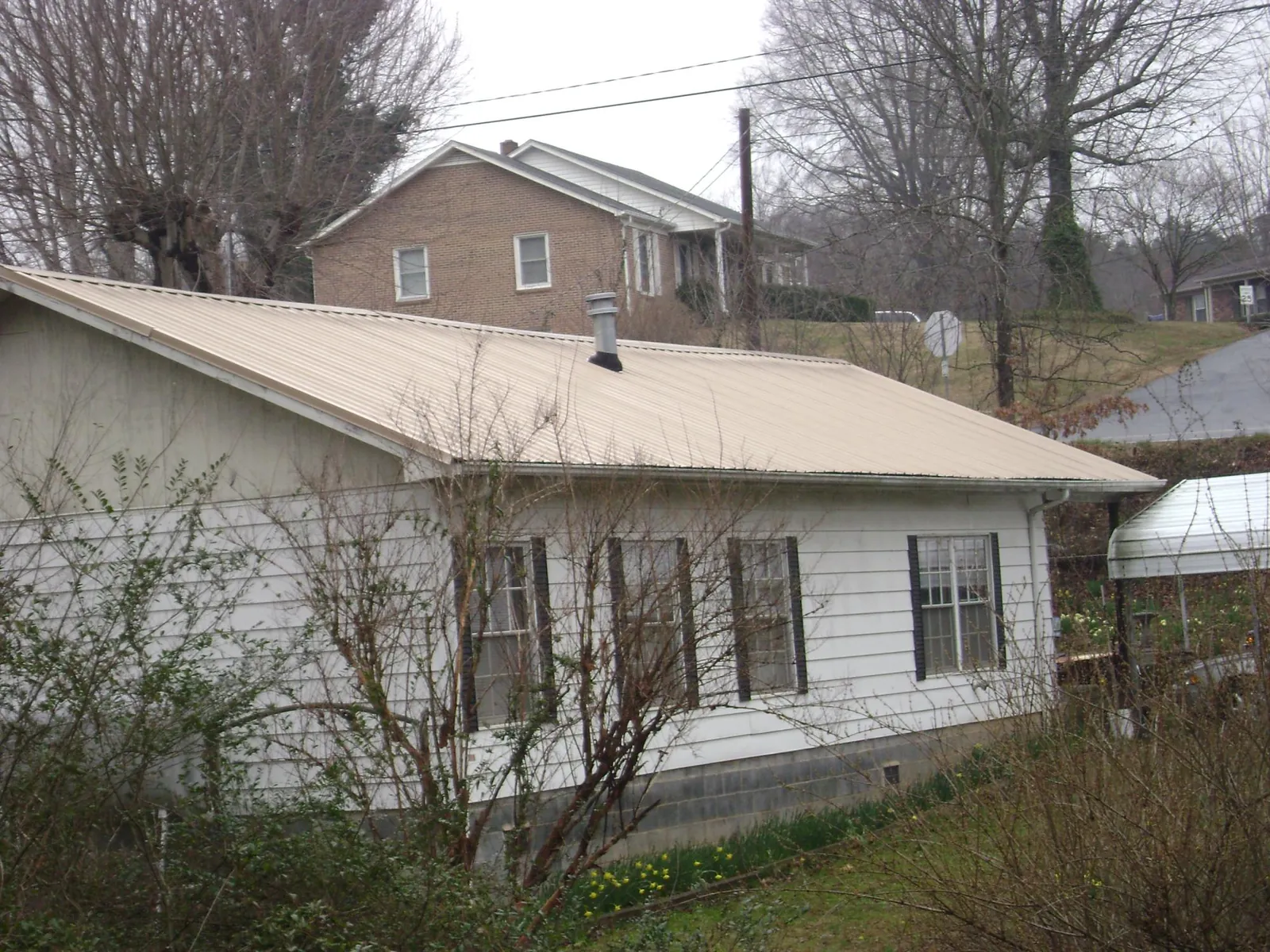 Tan metal roof on a white sided house set into a hillside — Commercial Roofing by Roofing Brothers in State Farm