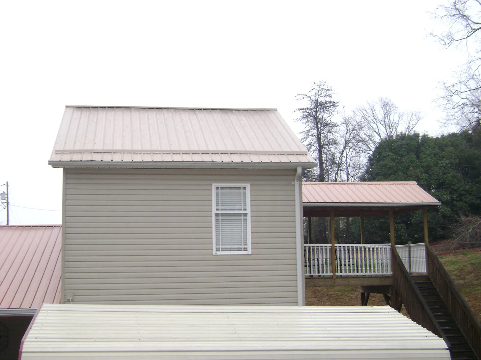 Tan metal roofs on a two story addition and attached porch, from a Roof Replacement job in State Farm
